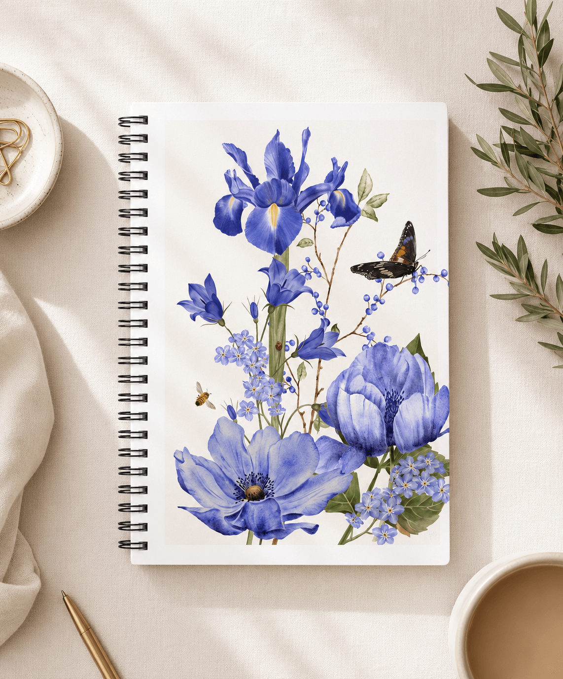 Top-down view of a spiral notebook with hand-painted blue iris, anemone, and bluebell floral design by Gabrielle Studio