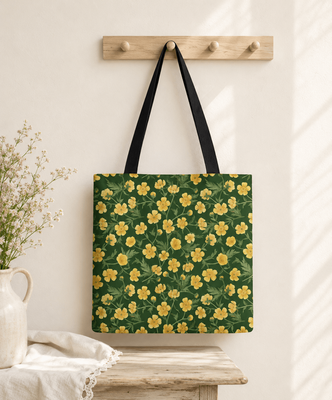 Green tote bag with an all-over hand-painted yellow buttercup pattern, hanging on a wooden peg rail