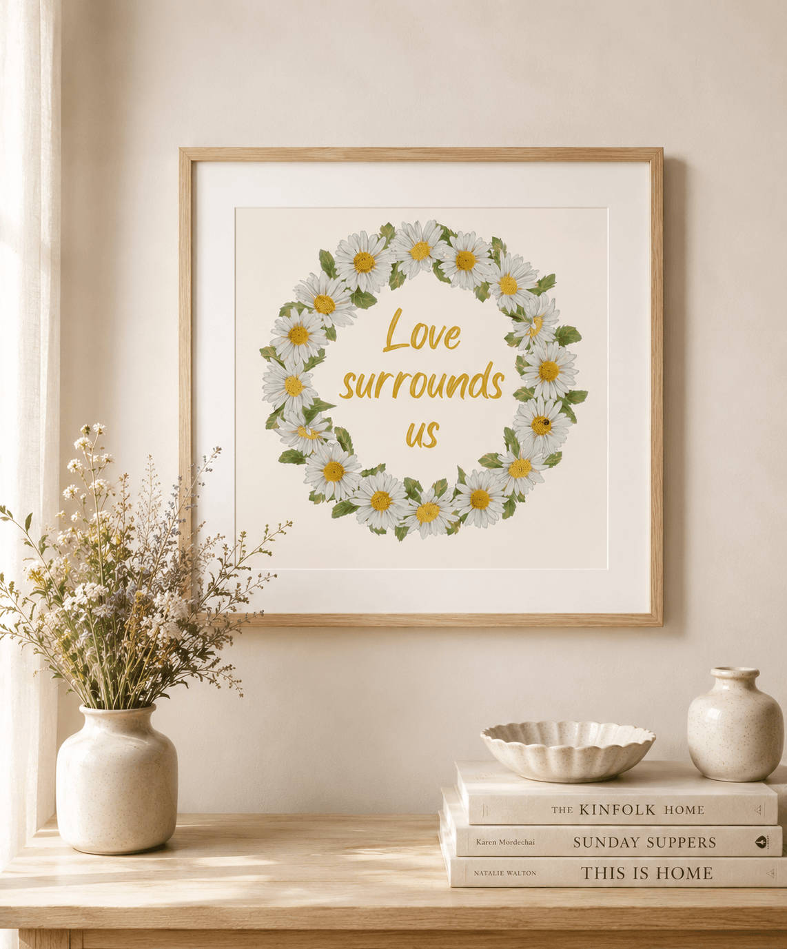Framed daisy wreath watercolour art print with the quote "Love surrounds us", above a console table