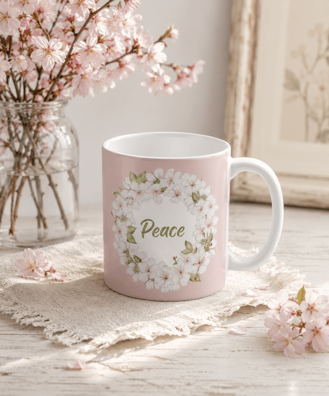 Pink mug with a cherry blossom wreath and "Peace" quote, styled with cherry blossom branches on a rustic wooden table