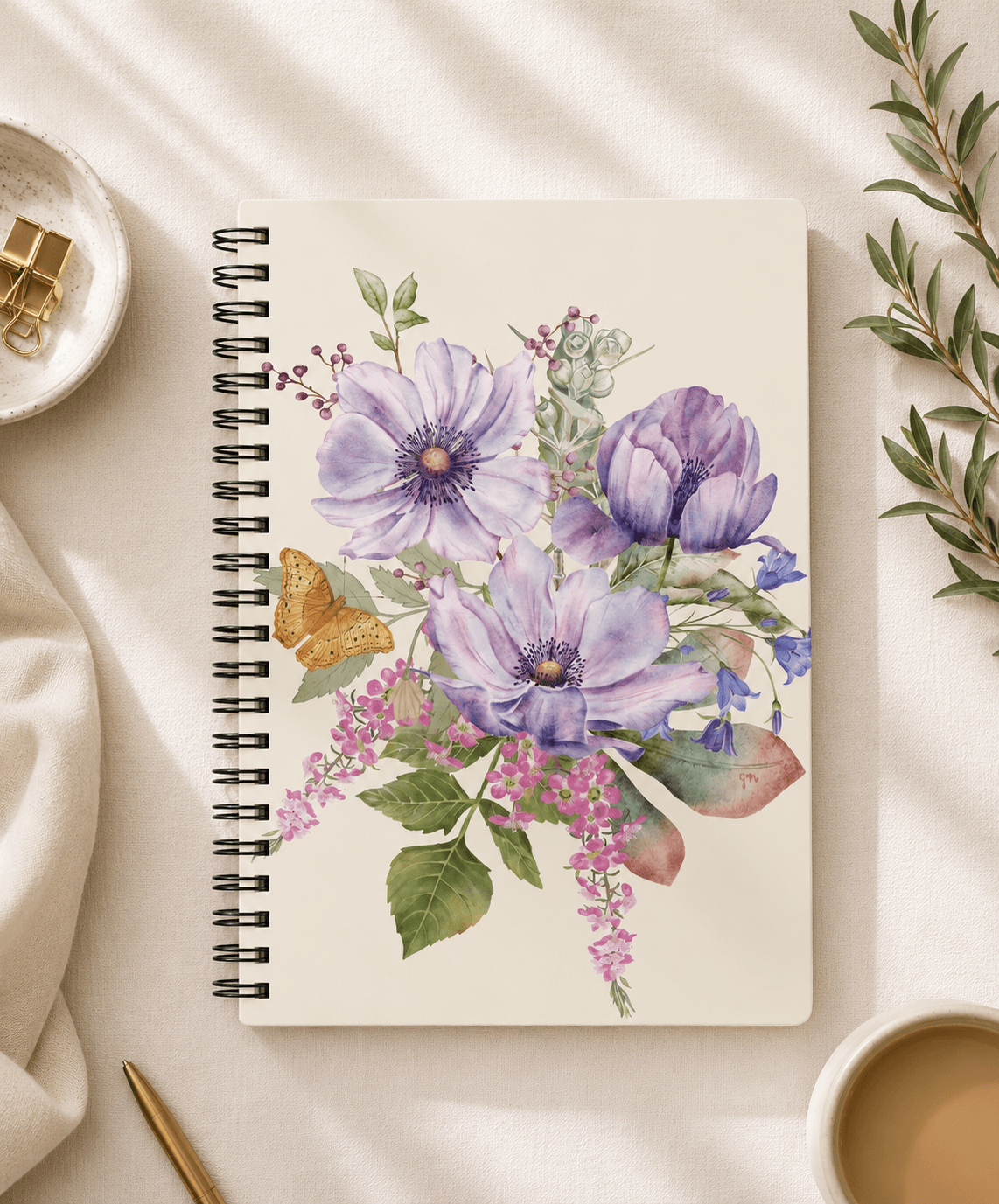 Top-down view of a spiral notebook with hand-painted purple anemone floral illustration and butterfly by Gabrielle Studio