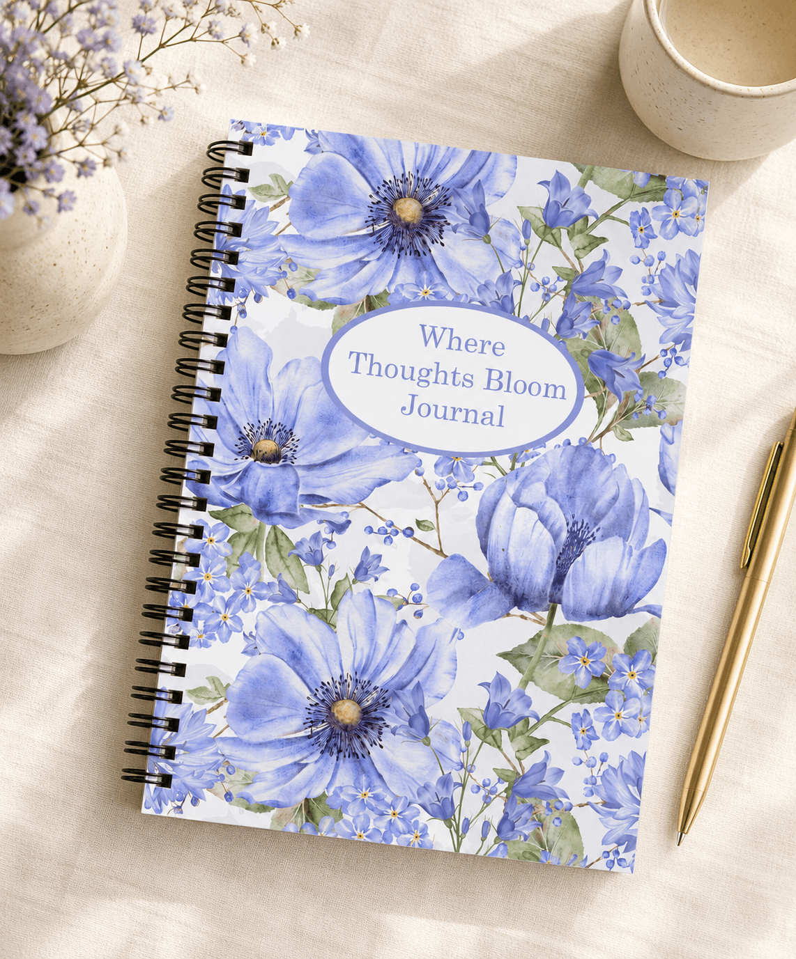Blue floral spiral-bound journal titled "Where Thoughts Bloom Journal" on a linen tablecloth with lavender and a ceramic mug