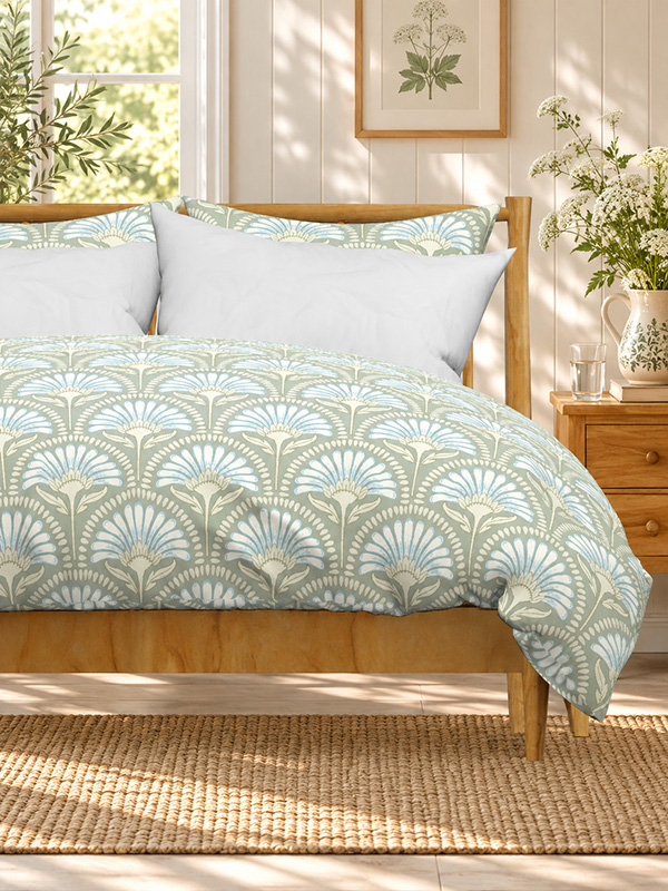 Bedroom with a wooden bed dressed in a sage green duvet cover patterned with art deco scallop daisies in soft blue and cream, beside a bedside table with wildflowers